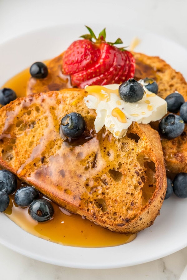 cropped close up air fryer french toast on a white plate with syrup and berries