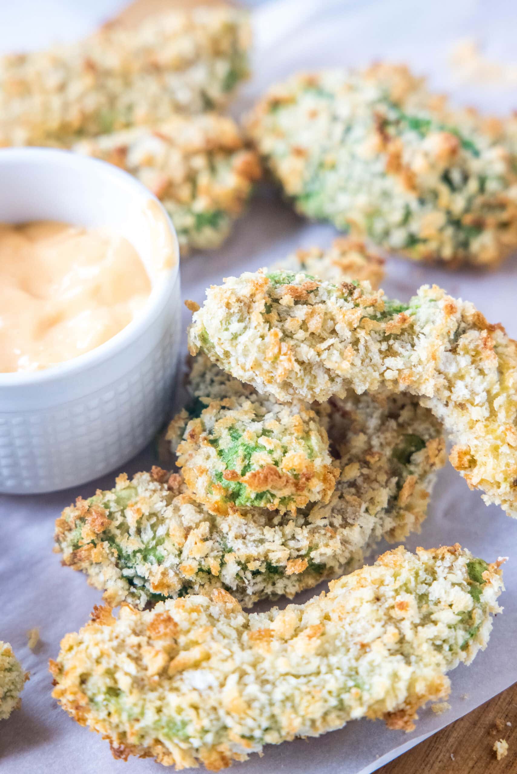 Avocado fries are crispy on the outside and warm and creamy on the inside, made in the air fryer (or oven). Don't forget the dipping sauce! Avocado fries on a wooden cutting board lined with parchment paper, next to a small bowl of dipping sauce.