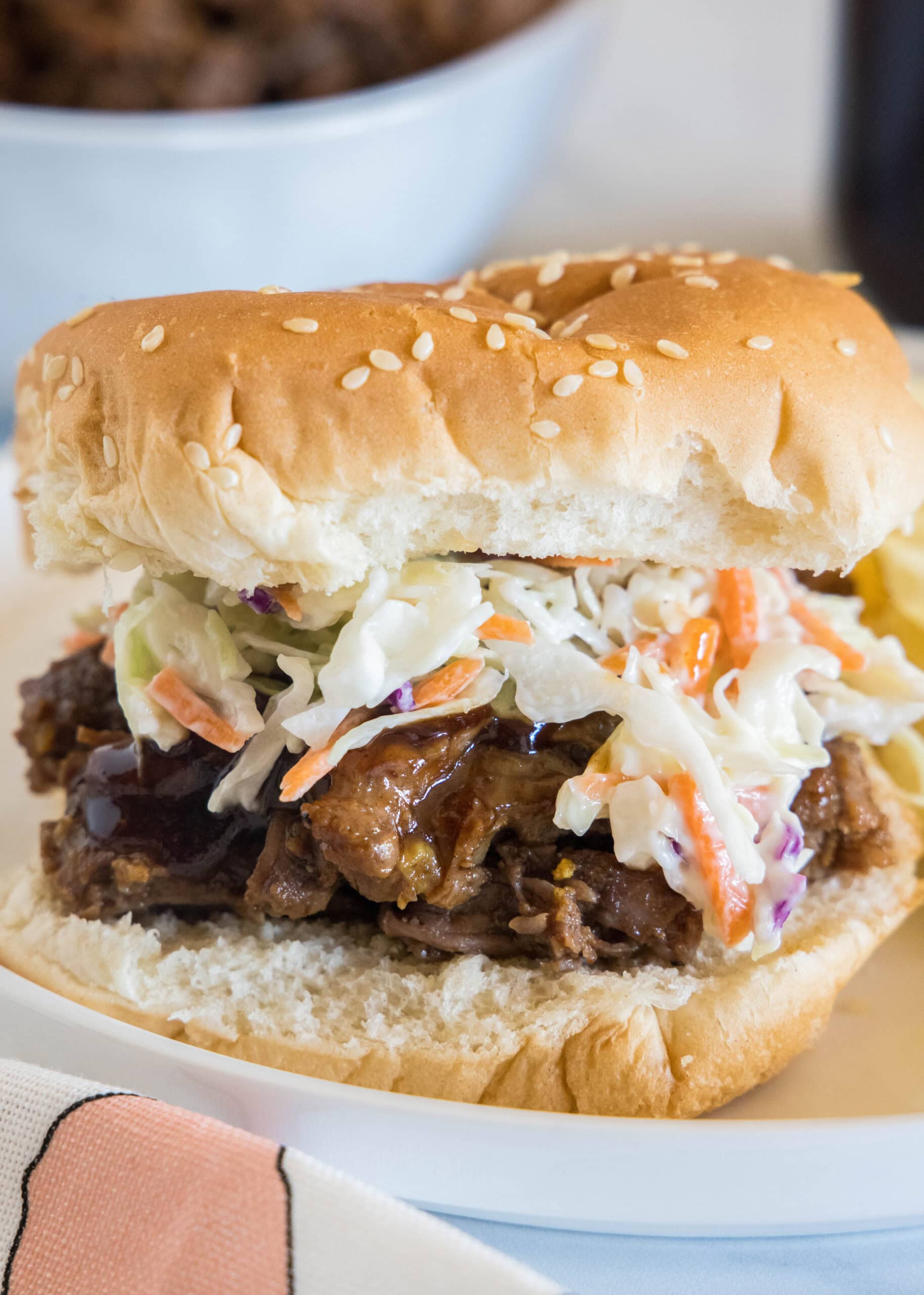This BBQ beef is slow-cooked until it’s fall-apart tender and tossed with sweet-tangy barbecue sauce. Perfect for a potluck or cookout! A BBQ beef sandwich with coleslaw on a white plate.