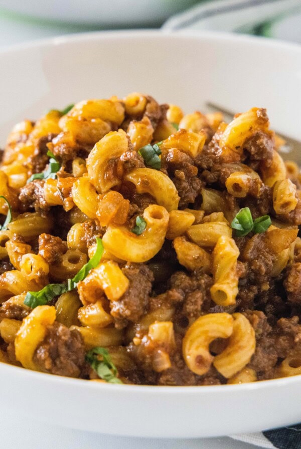 A white bowl with beefaroni and a fork