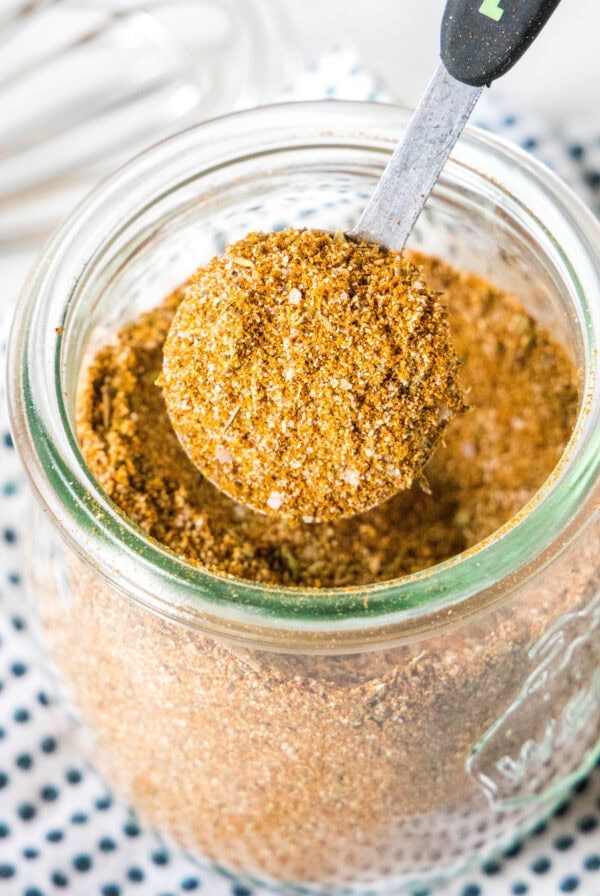 close up teaspoon of seasoning above a spice jar