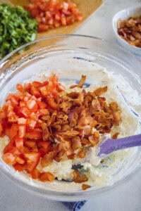 adding tomatoes and bacon to a mixing bowl