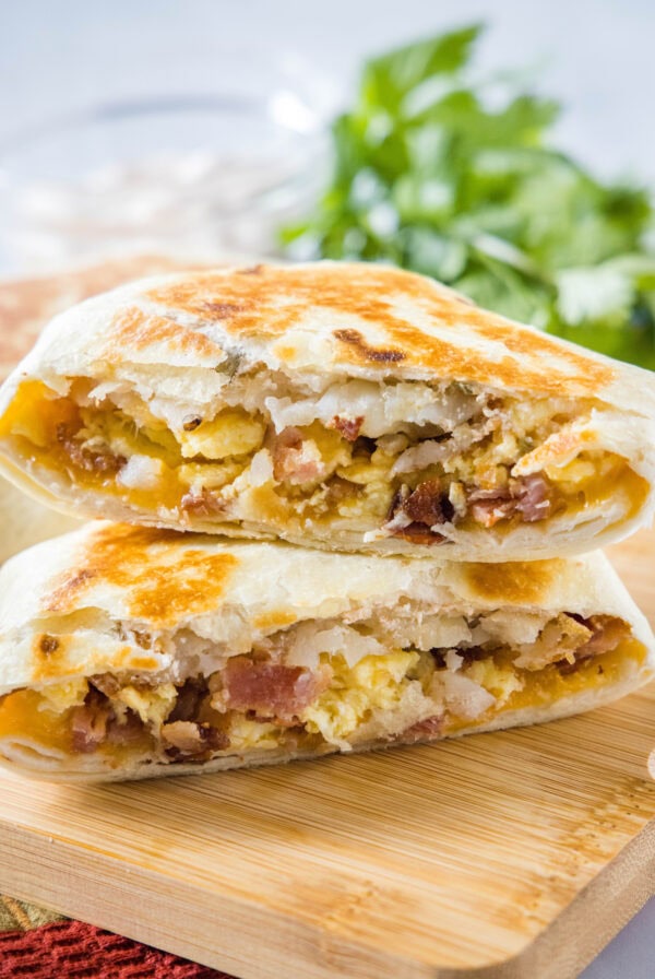 Two halves of a breakfast crunchwrap stacked on top of one another on wooden cutting board.