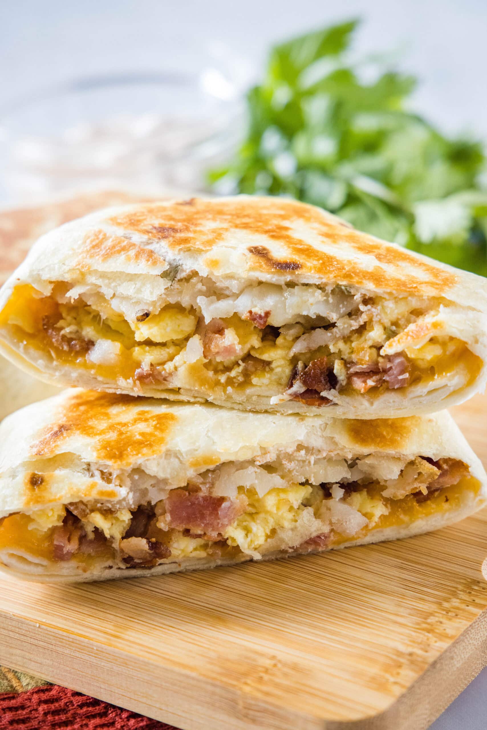 This copycat Breakfast Crunchwrap has crispy hashbrowns, eggs, bacon, and cheese layered with creamy jalapeño sauce inside a toasted tortilla. Two halves of a breakfast crunchwrap stacked on top of one another on wooden cutting board.