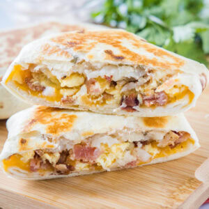 Two halves of a breakfast crunchwrap stacked on top of one another on wooden cutting board.