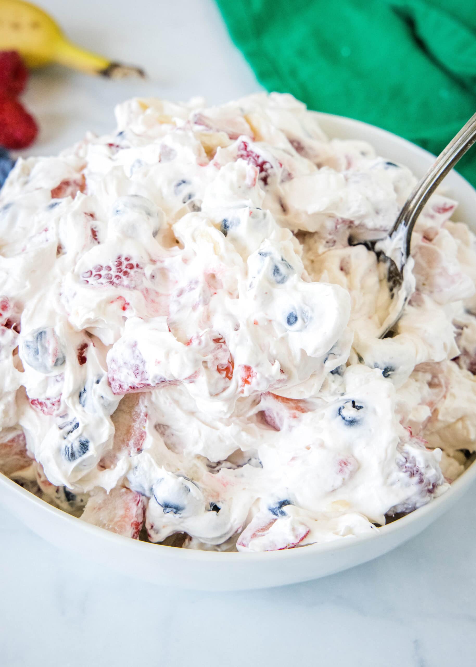 Cheesecake fruit salad is a cool and creamy side dish that doubles as dessert! Made with cream cheese, whipped topping, and fresh fruit. Cheesecake fruit salad in a bowl with a spoon for serving.