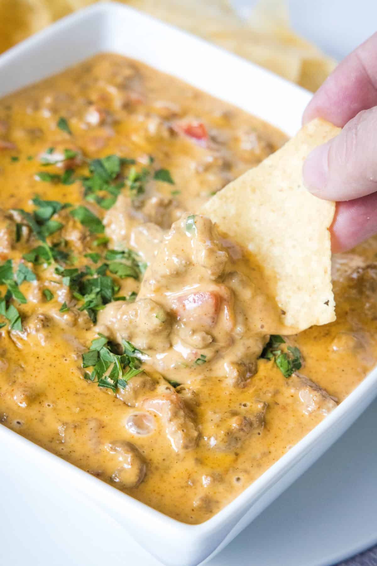 scooping cheesy rotel dip out of bowl with a tortilla chip