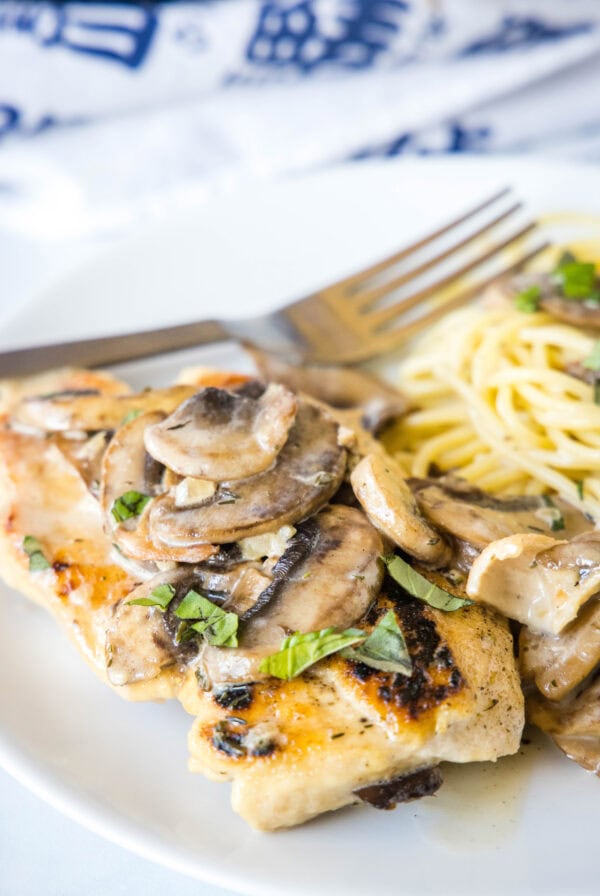 Chicken Marsala served with spaghetti on a plate next to a fork, topped with mushrooms.