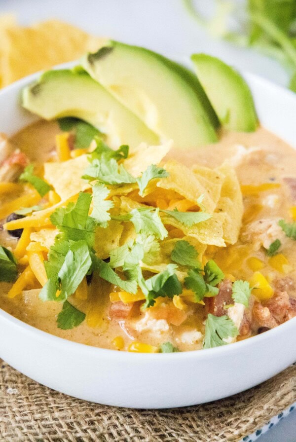 cropped image of chicken taco soup in a bowl with tortilla chips and cilantro