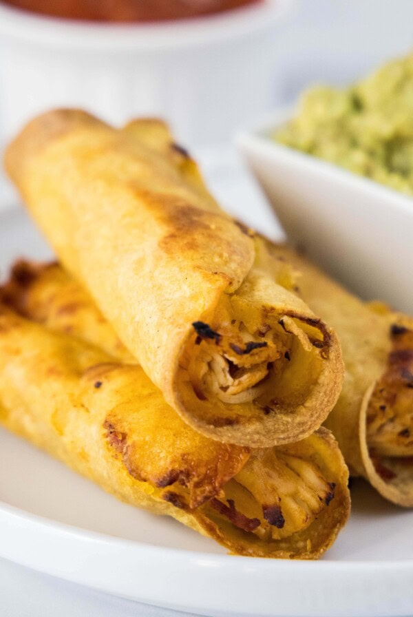 close up of crispy chicken taquitos on a plate with guacamole