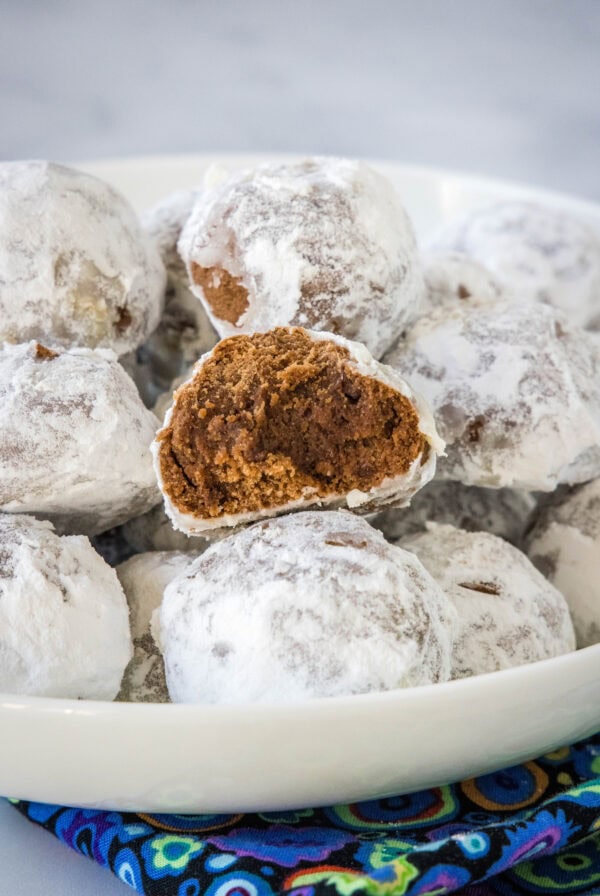 Chocolate snowball cookies staked on a white platter with a bite missing from one cookie.