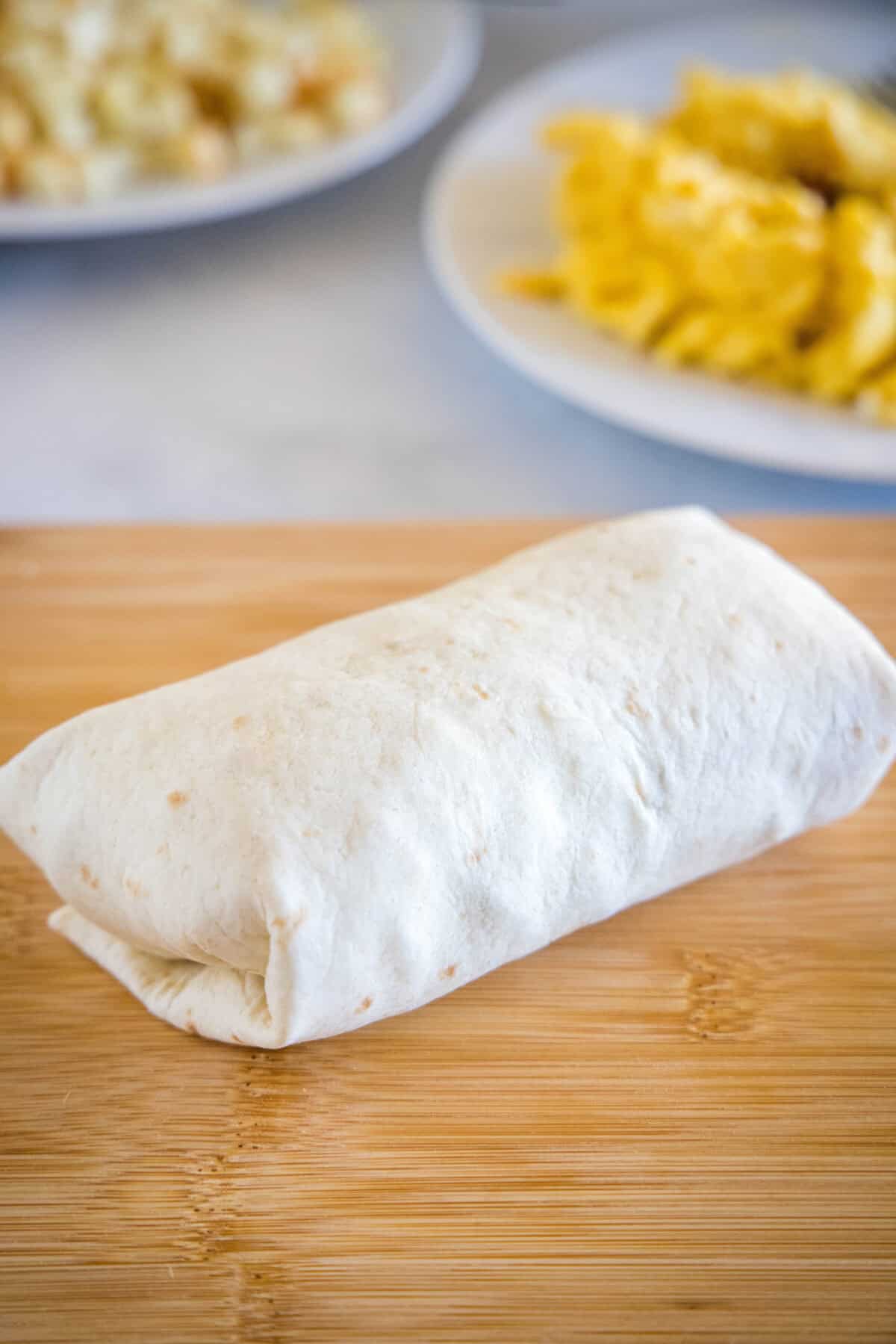 This chorizo breakfast burrito is a cheesy breakfast wrap loaded with crispy hash brown potatoes, spicy chorizo sausage, and fluffy eggs! A rolled up breakfast burrito on a wooden cutting board.