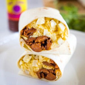 Two halves of a chorizo breakfast burrito stacked on a plate, showing the eggs, cheese, potatoes, and chorizo filling inside.