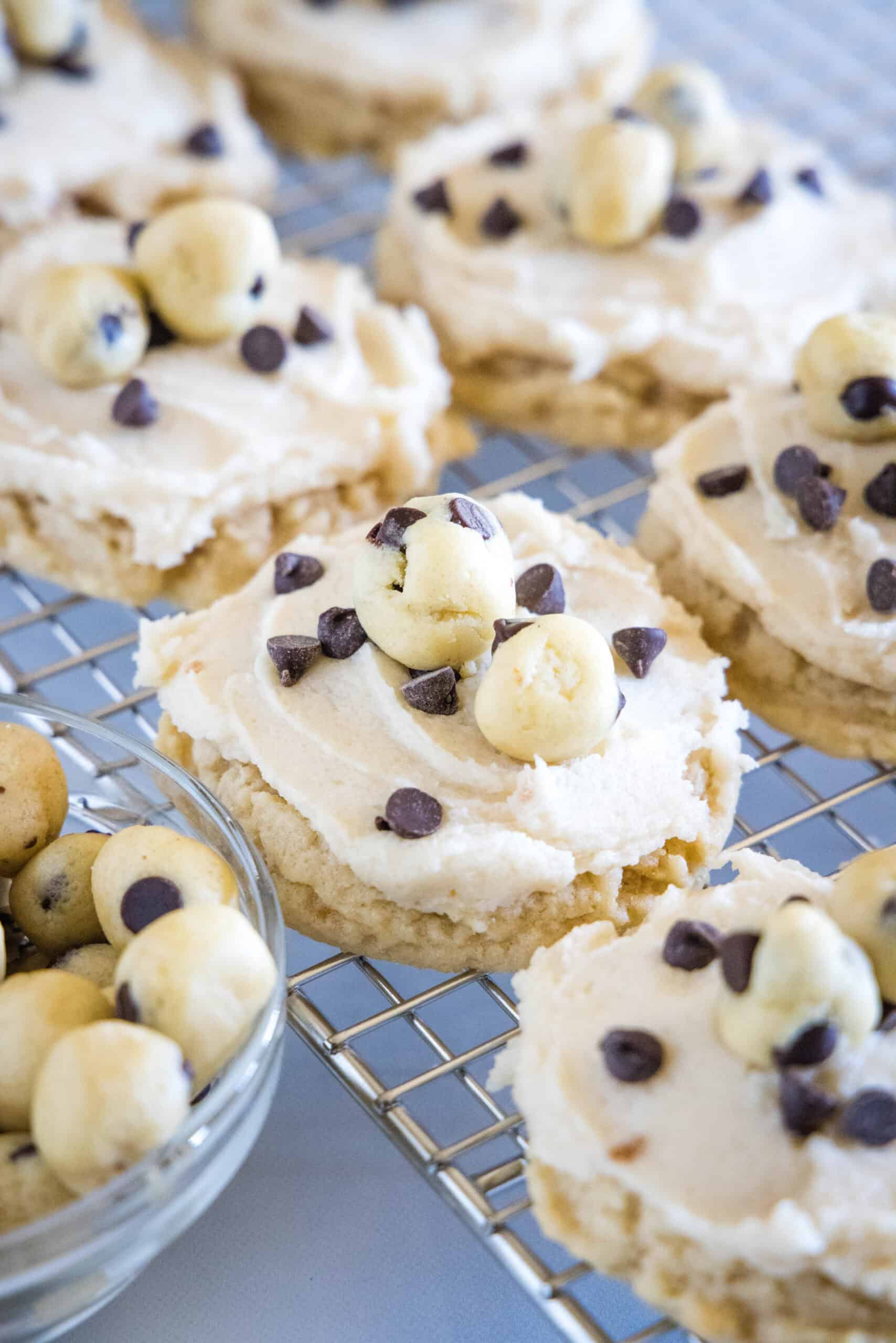 These cookie dough cookies are bakery-style sugar cookies topped with creamy cookie dough frosting, edible cookie dough, and chocolate chips! Frosted cookie dough cookies on a wire rack.