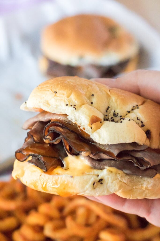holding beef & cheddar sandwich over a plate of curly fries