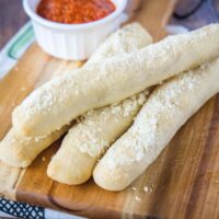 Four breadsticks on a cutting board with a ramekin of marinara sauce
