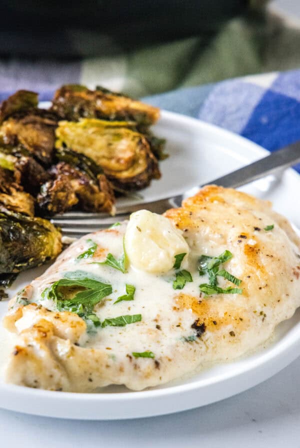 Creamy garlic chicken served with a side of roasted Brussels sprouts on a plate.