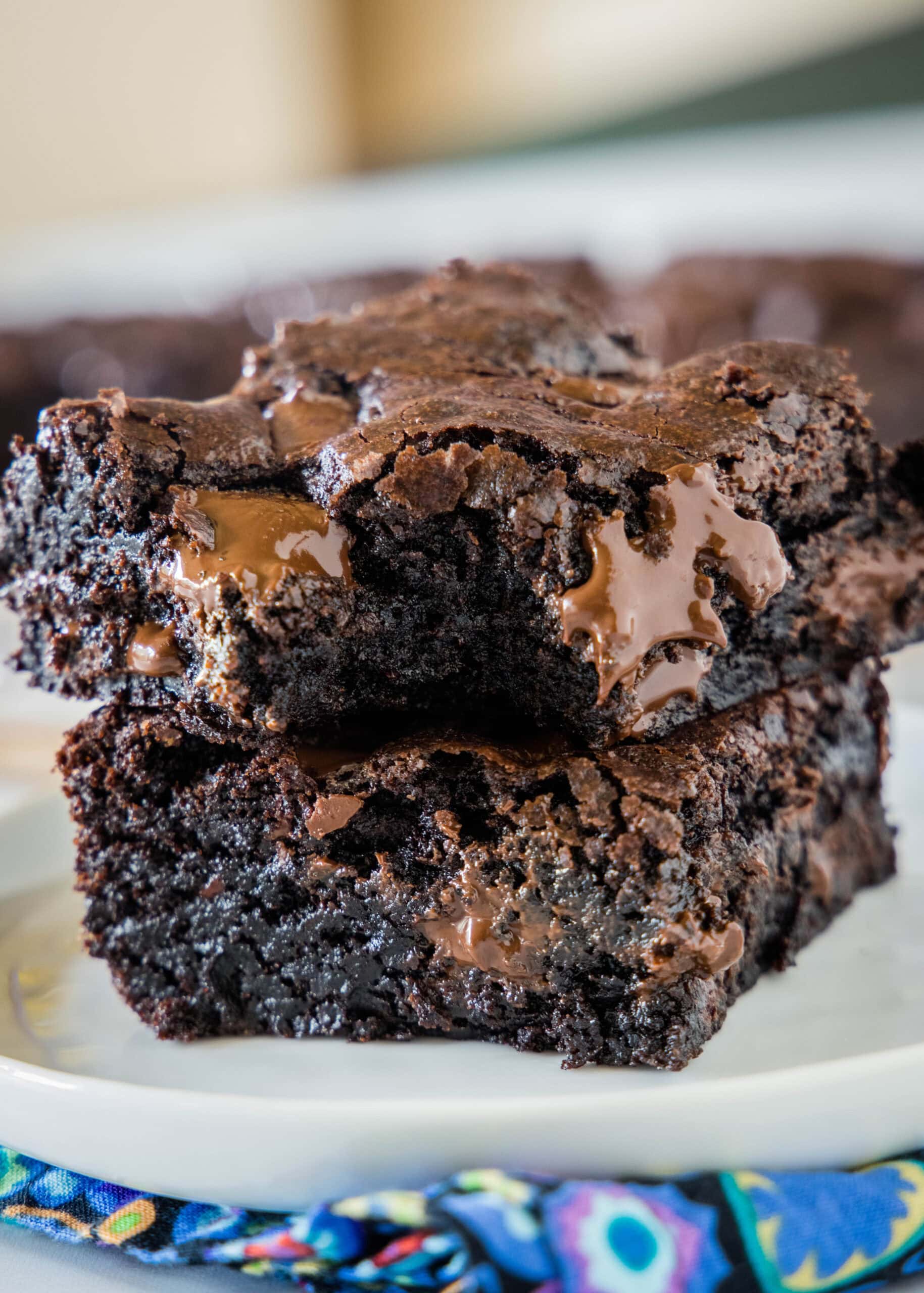 Make thick and chewy, fudgy double chocolate brownies with cocoa powder and chocolate chunks, for loads of melty chocolate in every bite! Two double chocolate brownies stacked on a plate with a bite missing from the top brownie.
