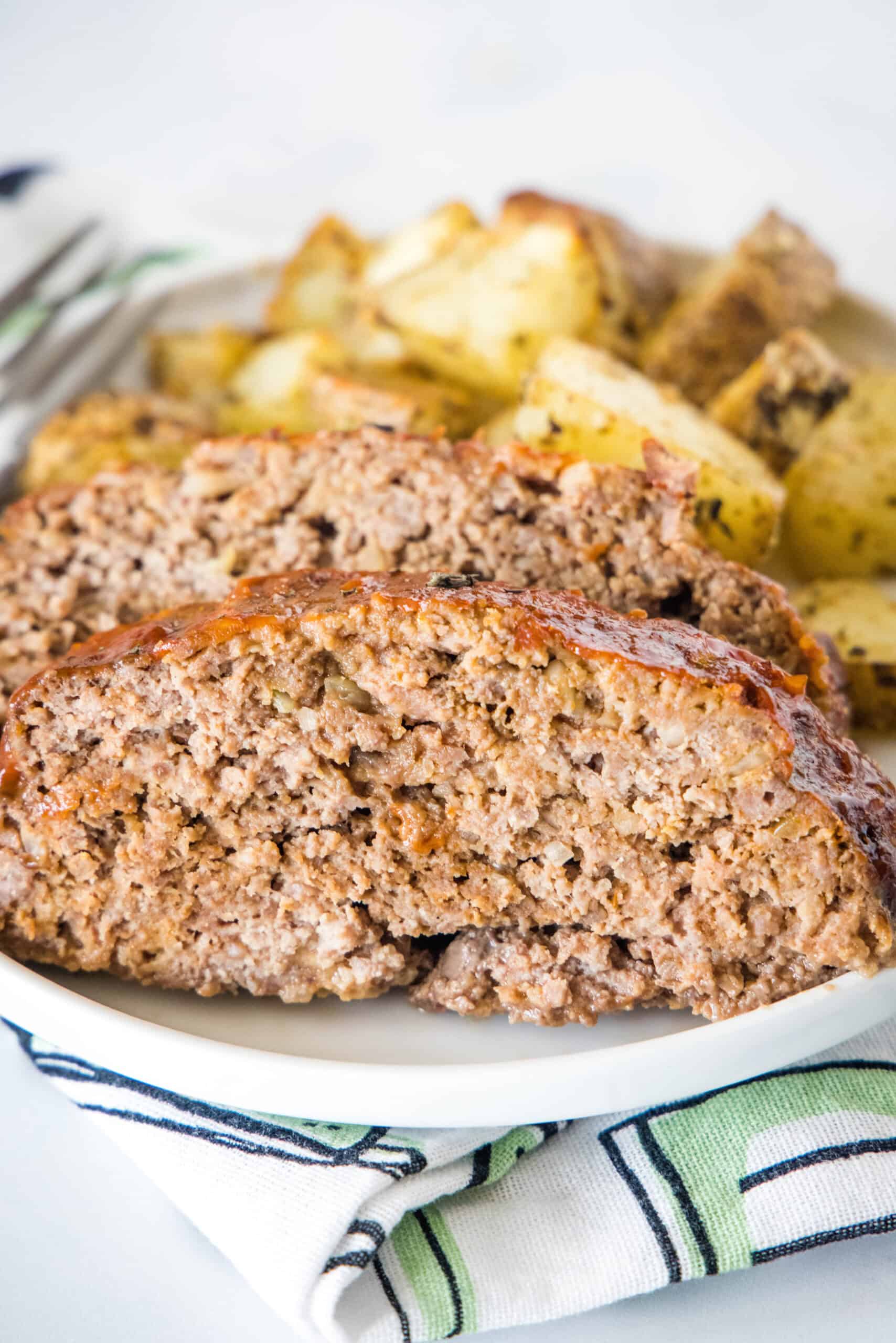 This 5-ingredient onion soup meatloaf is an easy recipe made with ground beef and savory onion soup mix, smothered with a sweet-tangy glaze. Onion soup meatloaf slices on a plate with roasted potatoes in the background.