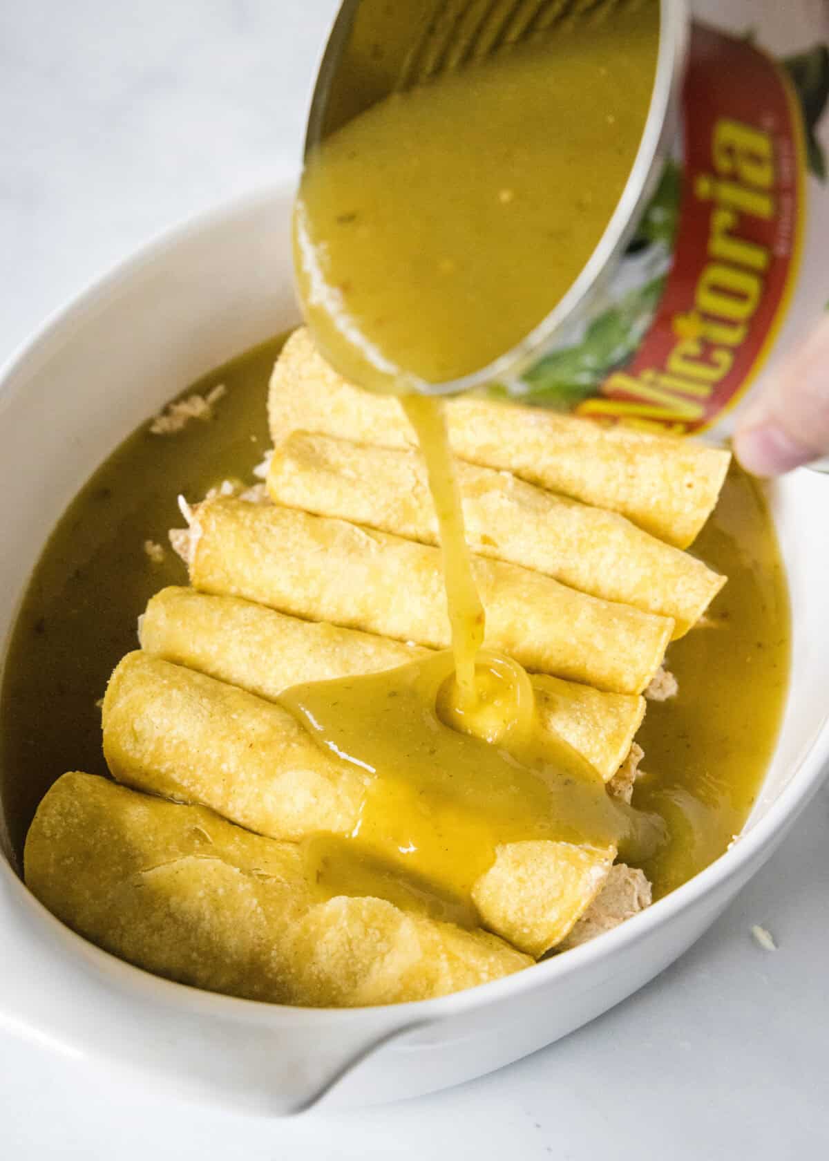 pouring enchilada sauce over rolled enchiladas in baking pan