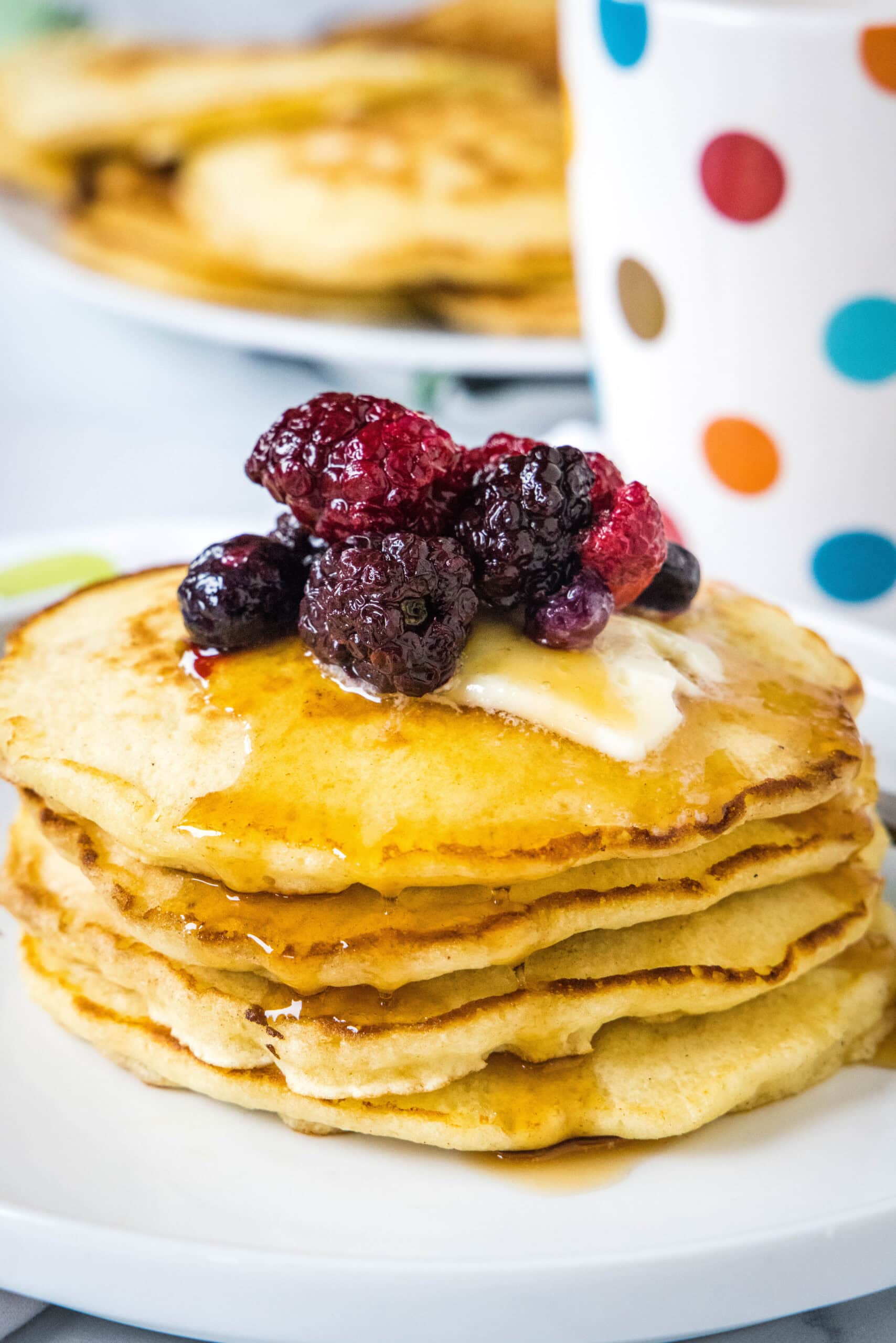 These griddle cakes are thick and fluffy old-fashioned pancakes fried to buttery perfection on the griddle, for an easy, cozy breakfast! A stack of griddle cakes topped with mixed berries and syrup on a white plate.