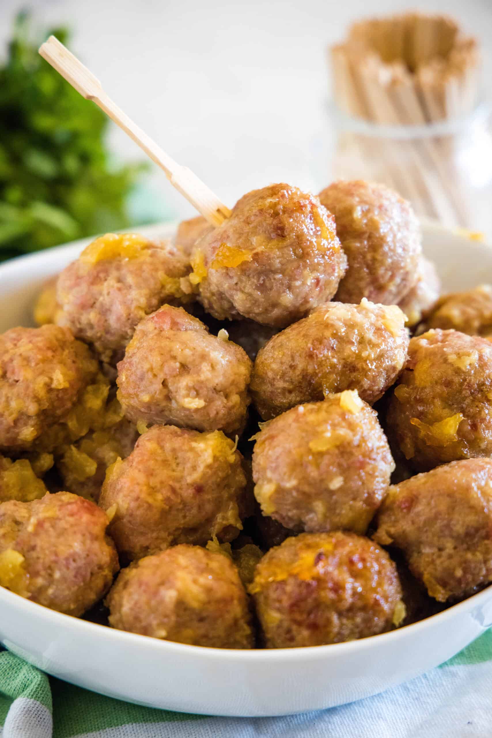This ham balls recipe is the ultimate party snack! They're super juicy and easy to make. Bake them with two different sauces, sweet or savory! Ham balls with pineapple sauce piled into a bowl with a jar of cocktail skewers in the background.