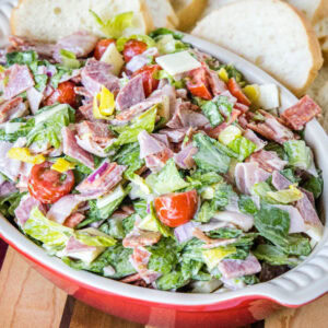 Hoagie dip in a red ceramic serving bowl with bread slices in the background.