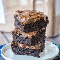close up stack of frosted brownies on white plate