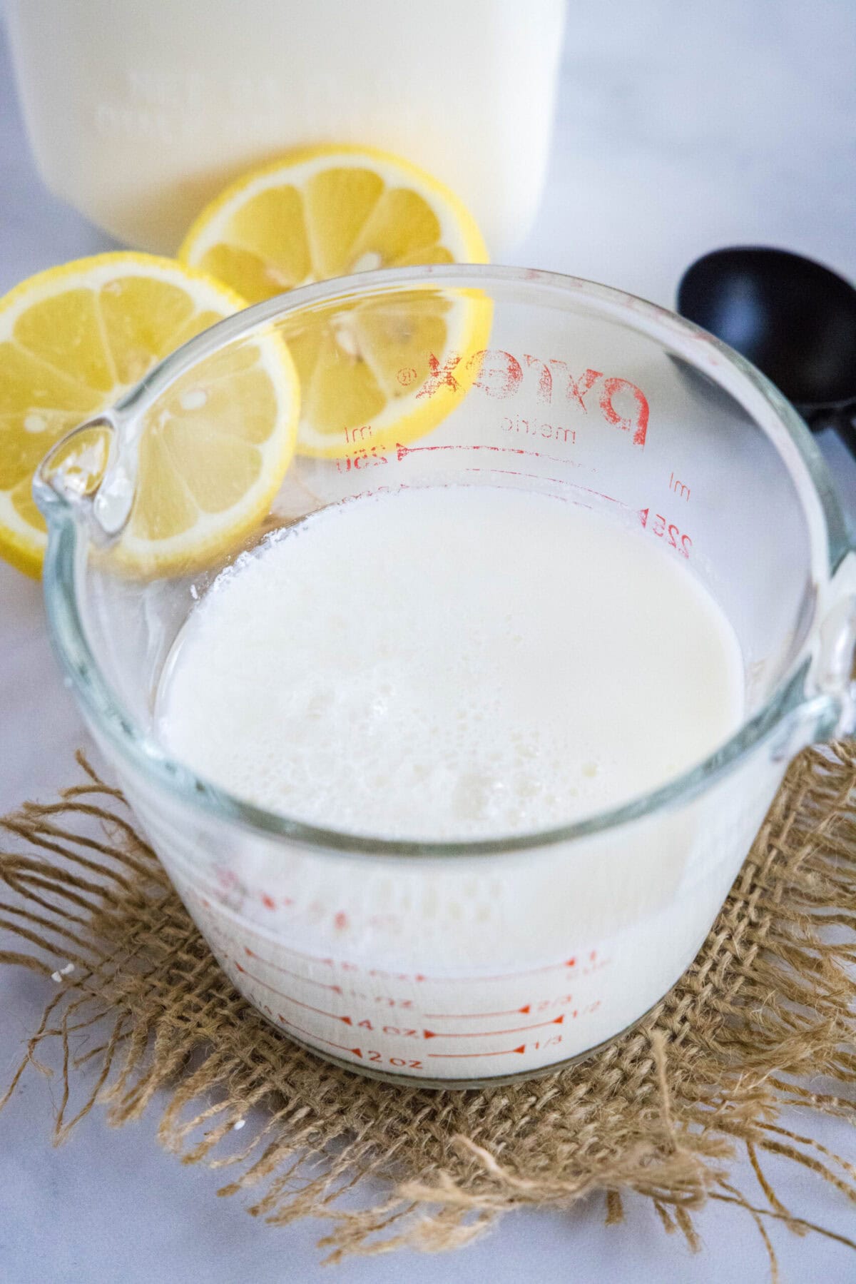 This 2-ingredient homemade buttermilk recipe is super creamy, perfectly tangy, and can be used in any recipe that calls for buttermilk. A pyrex of buttermilk with lemon slices in the background
