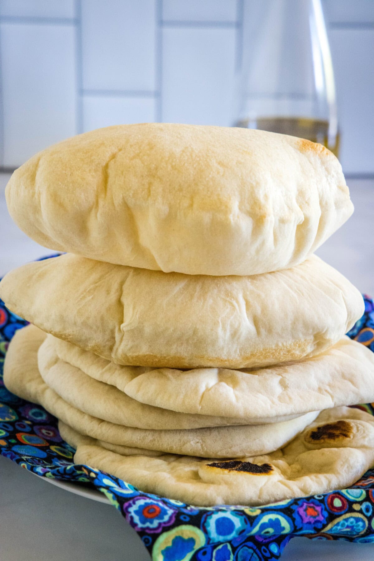 Fluffy homemade pita breads stacked on a blue cloth.