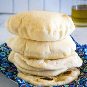 Fluffy homemade pita breads stacked on a blue cloth.