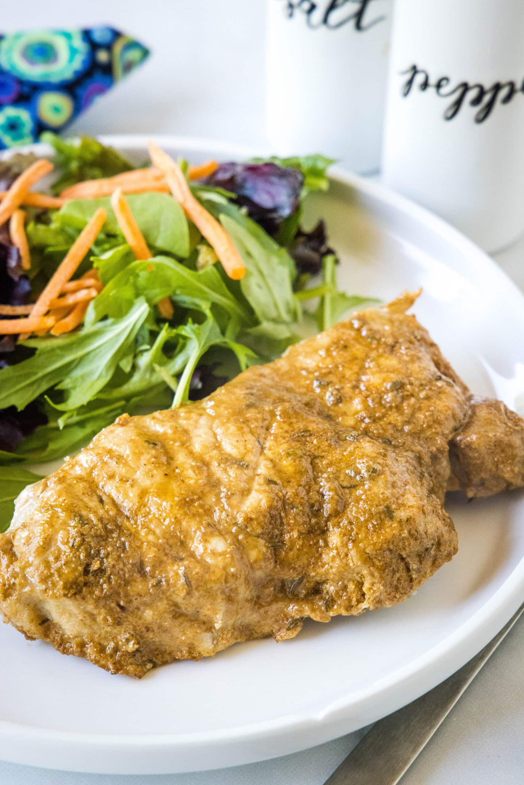 Instant Pot pork chops are perfectly seasoned, perfectly cooked, and so juicy! Pair these easy pork chops with a side of veggies or salad. An instant pot pork chop with a side of salad on a white plate.