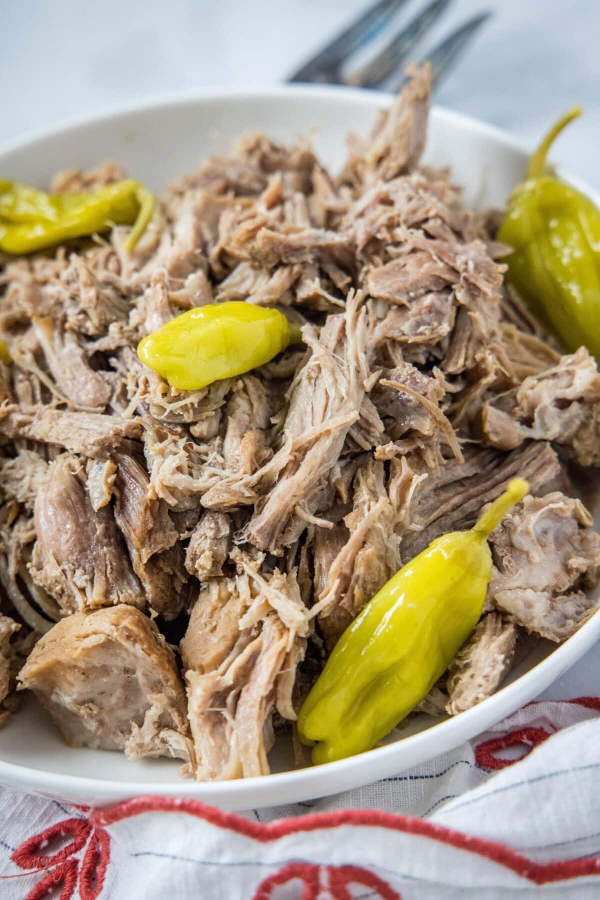 Mississippi pork roast is full of juicy and tender meat with spicy pepperoncini peppers, and it's so rich, savory, creamy, and buttery. A bowl of shredded pork with pepperoncini peppers, next to a fork