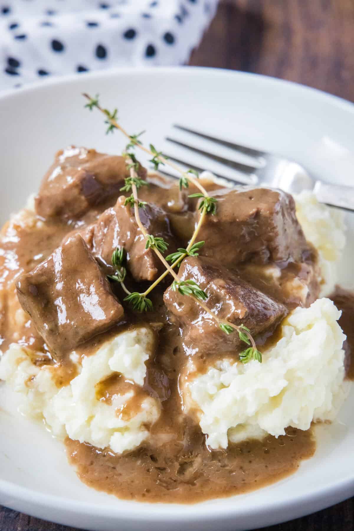 beef tips and gravy over mashed potatoes in a white bowl