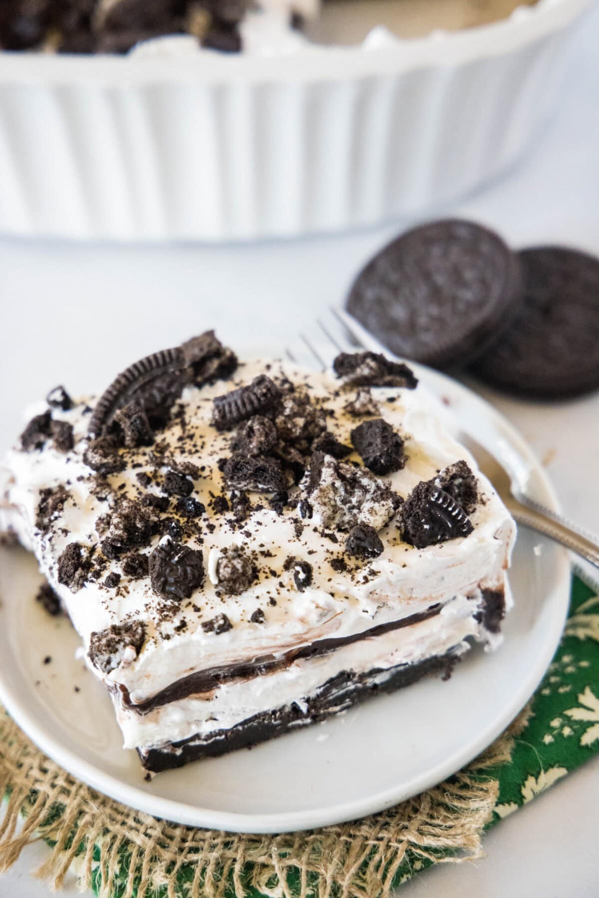 These 30-minute no bake Oreo cream squares are loaded with crumbled cookies, chocolate, pudding, cream cheese, and Cool Whip. Overhead view of a slice of Oreo squares on a plate, topped with crumbled Oreos, next to a few Oreos