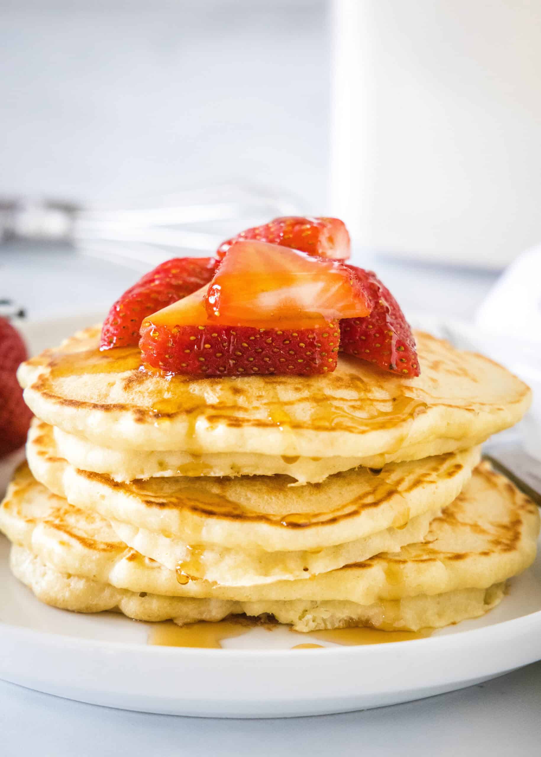 My homemade pancake mix needs only 5 ingredients! Whisk it together and keep this mix in the pantry for irresistibly fluffy pancakes anytime. A stack of homemade pancakes topped with fresh strawberries and syrup on a white plate.