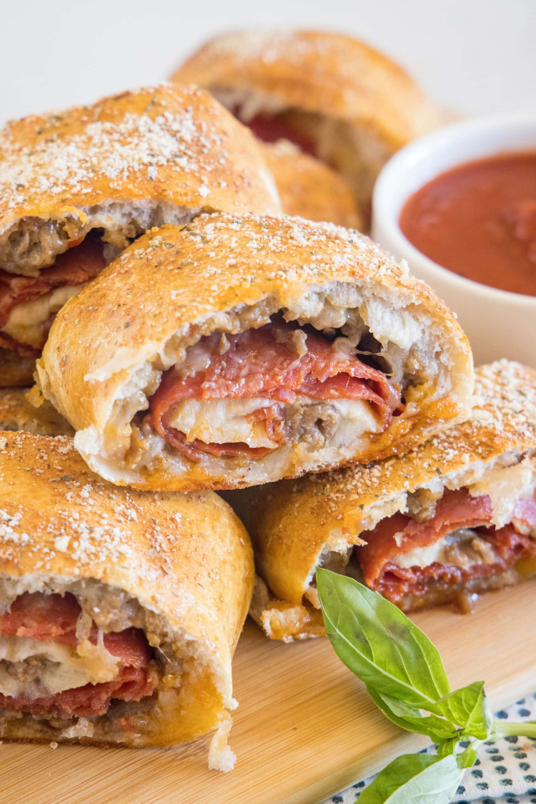 Put a fun spin on pizza night with this easy pizza bread recipe. Roll your favorite pizza toppings inside a pizza crust, bake, and slice! #pizzabread #pizza Pizza bread slices stacked on a wooden board next to a bowl of pizza sauce for dipping.