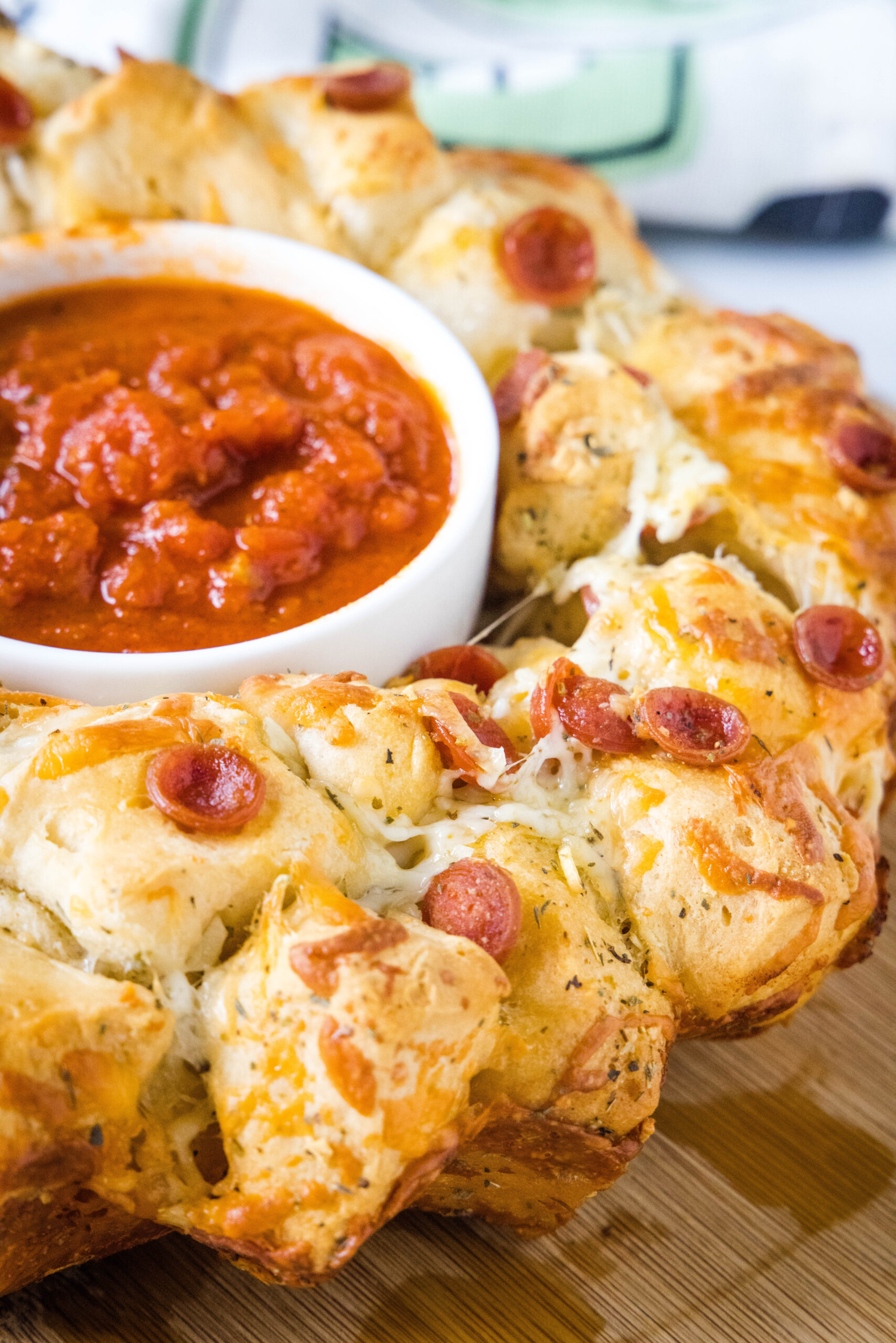 Pizza monkey bread is an easy, pull-apart-style appetizer or dinner made from puffy biscuits baked with pepperoni and lots of melty cheese! Pizza monkey bread with a bowl of pizza sauce in the middle hole.
