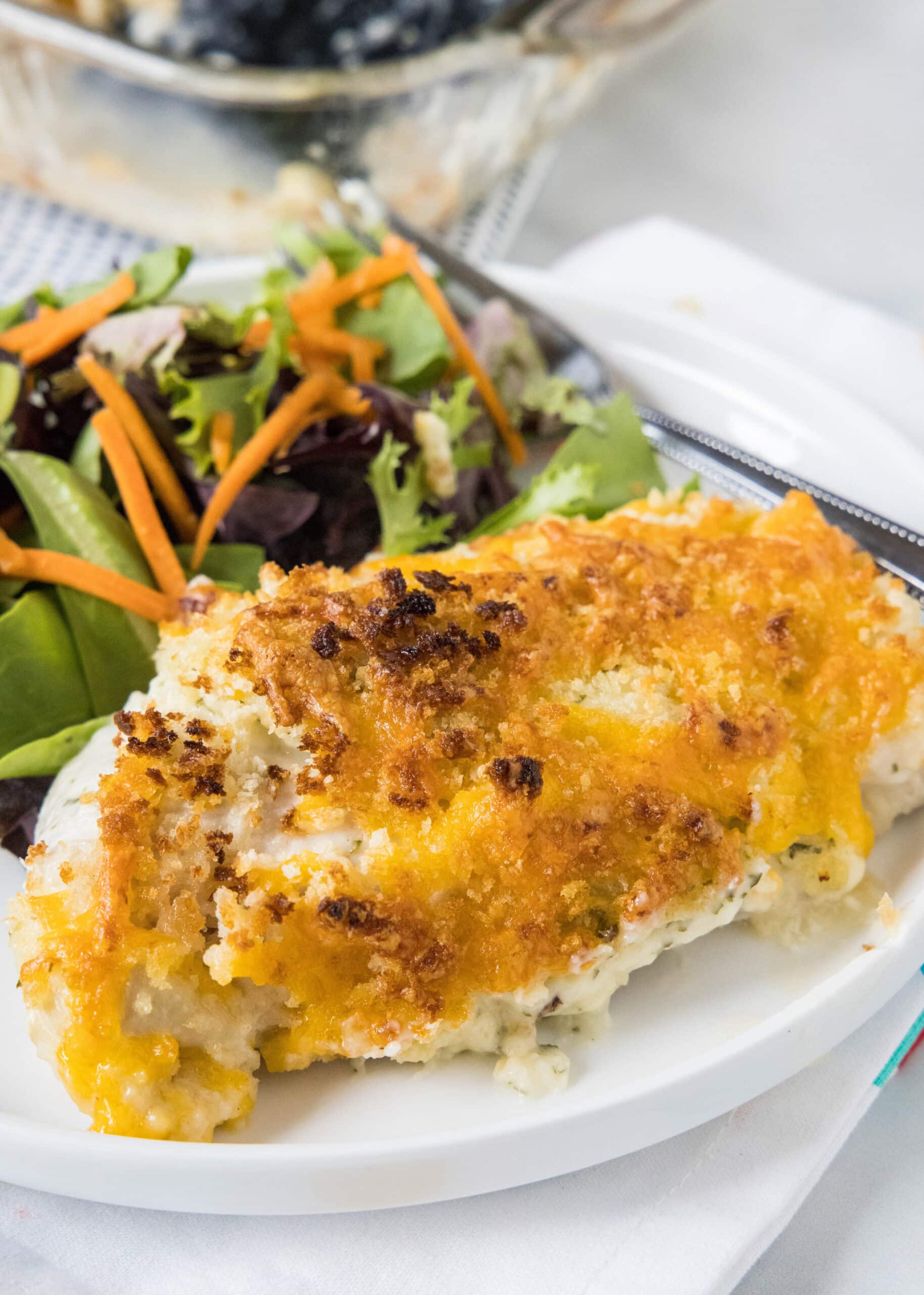 Baked ranch chicken is an easy dinner with juicy chicken coated in ranch and baked under crispy breadcrumbs with plenty of melted cheddar! Baked ranch chicken served with a side of salad on a white plate.