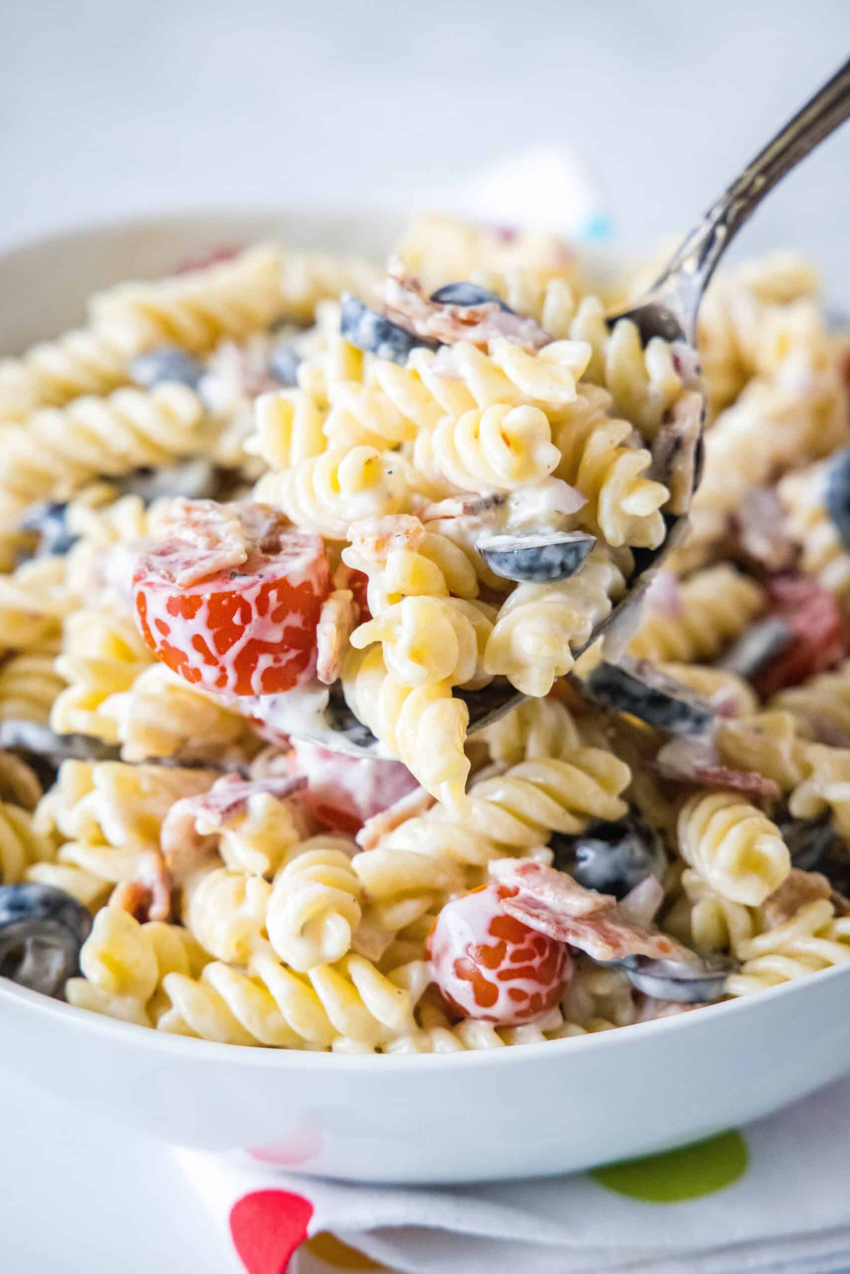 This ranch pasta salad is an easy summer side dish packed with crispy bacon, veggies, and pasta tossed in creamy buttermilk ranch dressing. A large serving spoon scooping ranch pasta salad from a white bowl.