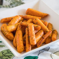 Seasoned roasted carrots in a square white bowl.