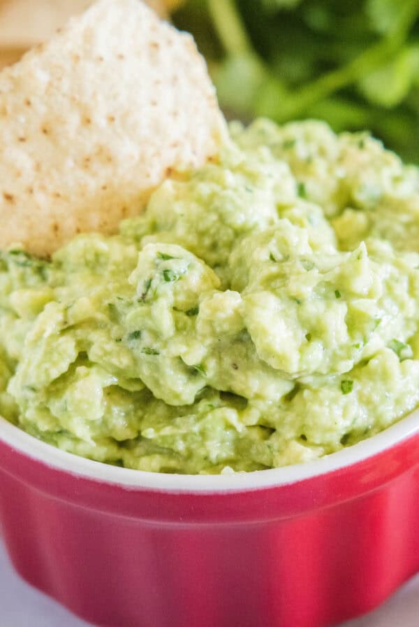 cropped close up roasted garlic guacamole in a bowl with a tortilla chip