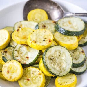 Roasted zucchini and squash in a bowl with a serving spoon.