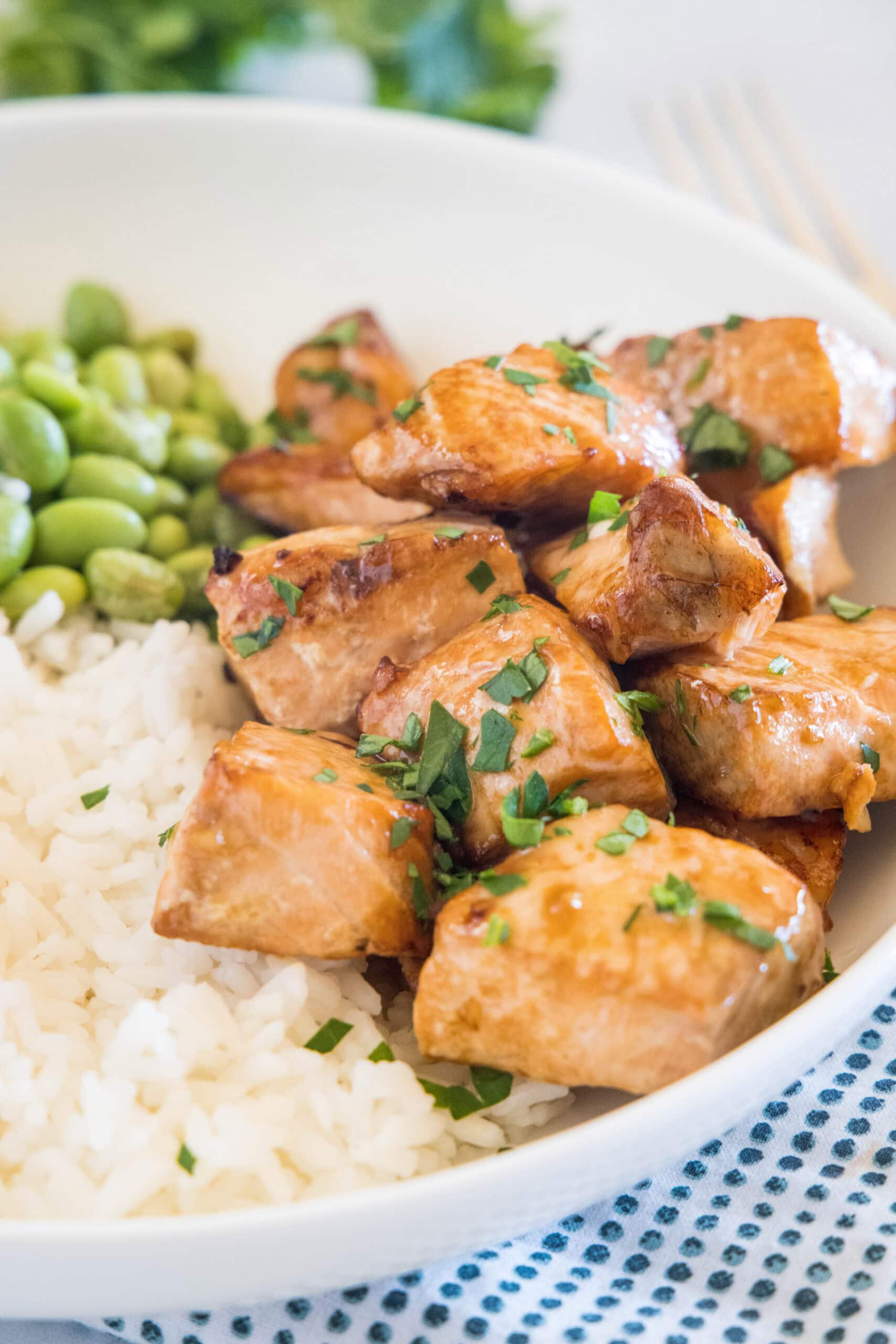 Juicy air fryer salmon bites are packed with flavor thanks to an easy soy marinade, and ready for a rice bowl or salad in under 15 minutes! #airfryer #salmonbites #salmon Salmon bites served with rice and edamame beans in a white bowl.