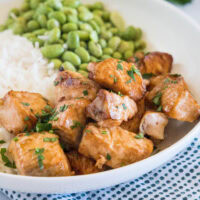 Salmon bites served with rice and edamame beans in a white bowl.