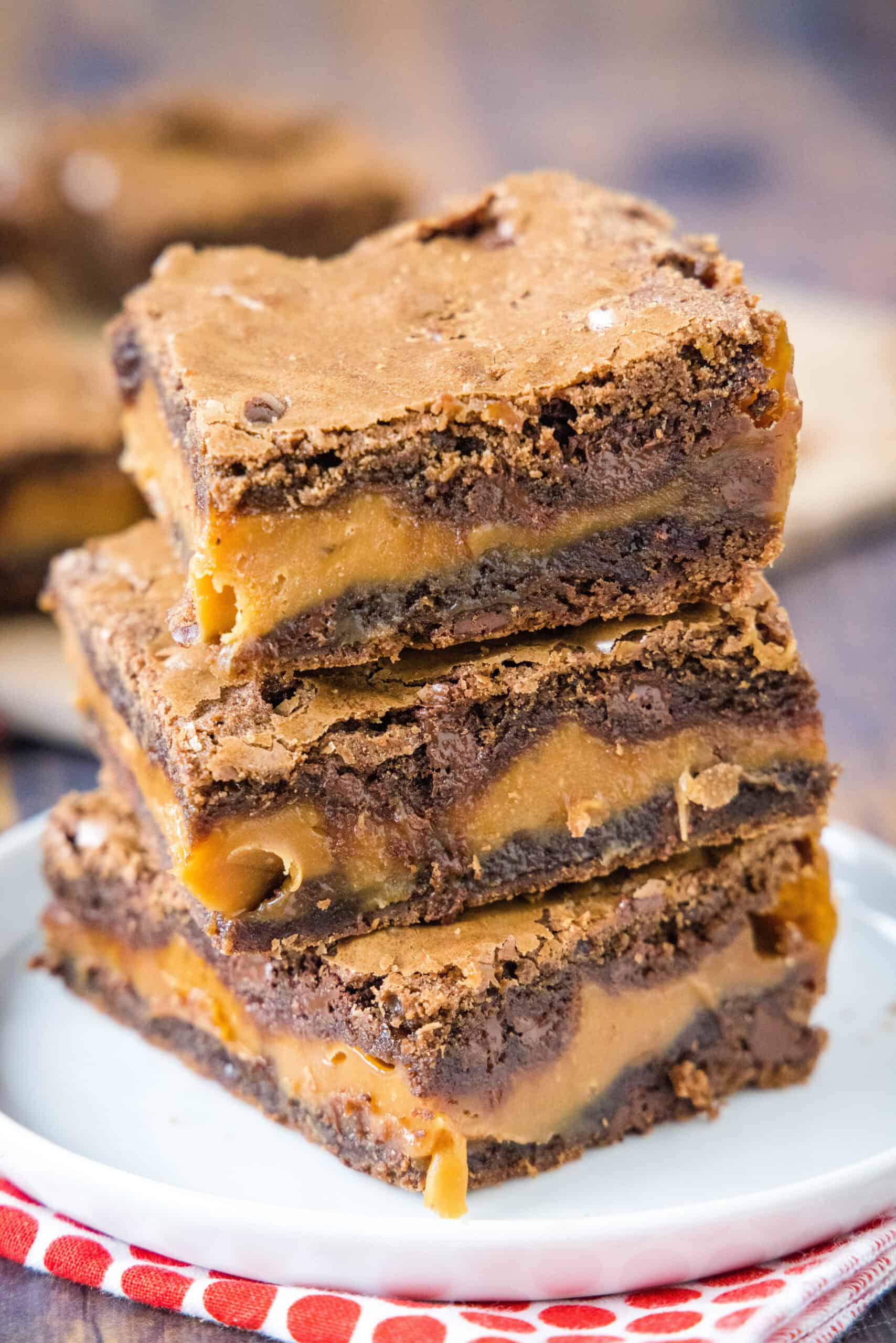 These irresistible salted caramel brownies are rich, fudgy chocolate brownies filled with a thick layer of gooey, melty caramel in the middle! Three salted caramel brownies stacked on a white plate.