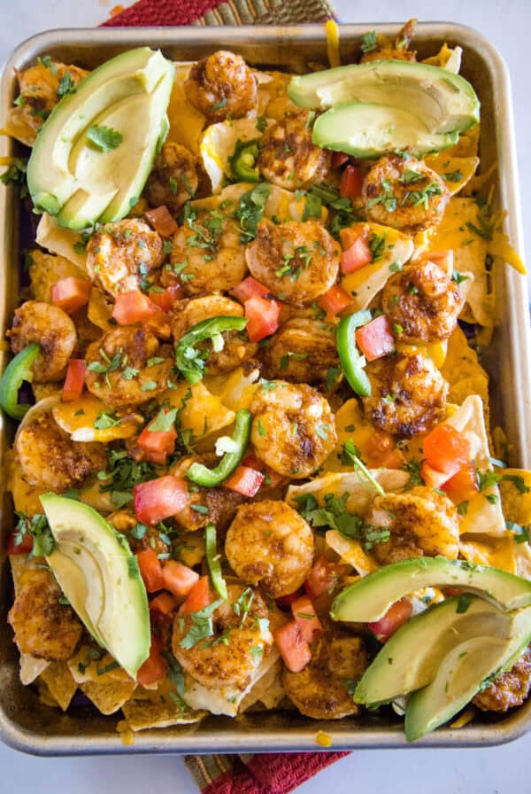 Overhead view of shrimp nachos on a sheet pan garnished with avocado slices.