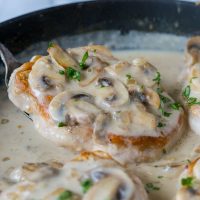 Close up of smothered pork chops with mushroom gravy in a skillet.