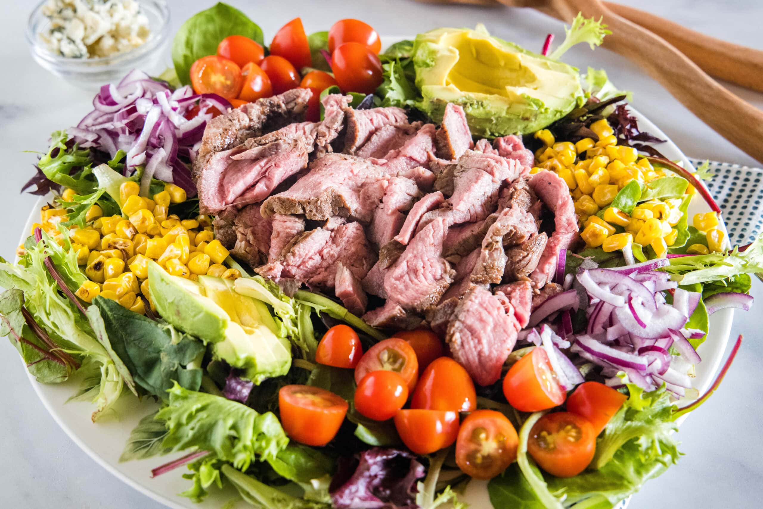 This easy steak salad recipe with fresh summer veggies, avocado, blue cheese, and creamy balsamic dressing is perfect for grilling season! Steak salad served on a large platter.