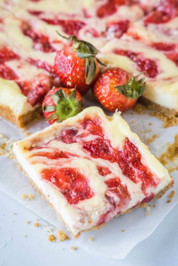 Close up of a strawberry cheesecake bar with fresh strawberries and more bars in the background.